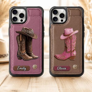 May include: Two smartphone cases with leather-like textures. The left case is mauve with a brown cowboy hat and boots graphic and the name Emily. The right case is brown with a pink cowboy hat and boots graphic and the name Olivia.