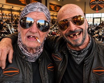 May include: Two individuals wearing black leather motorcycle jackets with orange and black hexagonal patches on the chest. Both wear gold-rimmed aviator sunglasses. One wears a grey patterned head covering and the other a black and white bandana.