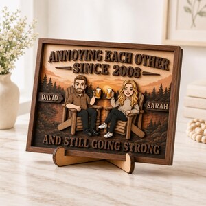 May include: A rectangular wooden framed sign featuring a layered 3D design of two people sitting in chairs holding beer mugs. The text reads ANNOYING EACH OTHER SINCE 2008, DAVID, SARAH, and AND STILL GOING STRONG against a forest and sunset background.