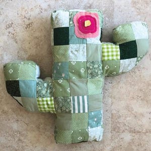 May include: A patchwork cactus toy made from various green fabric squares, with a pink and yellow flower accent. The text "PATCHWORK CACTUS TOY" and "A quilt pattern by Kirious Design Co." are at the top. The bottom features the Kirious Design Co. logo and contact information.