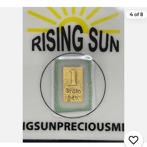 May include: A small rectangular gold bar labeled 1 Grain 24K, encased in a clear plastic protective sleeve. The sleeve is mounted on a white card featuring a yellow sun graphic and the black text RISING SUN at the top and IGSUNPRECIOUSME at the bottom.