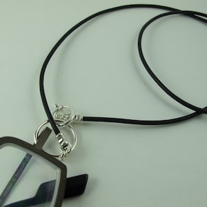 May include: Black eyeglass chain with a silver clasp and a pair of glasses with a black frame and clear lenses. The glasses have the text "The Marco D. Belgium" printed on the lenses.