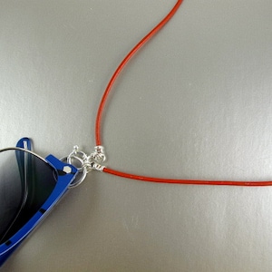 May include: A pair of blue sunglasses with a red cord attached to the frame. The cord is looped around the sunglasses and can be worn around the neck.