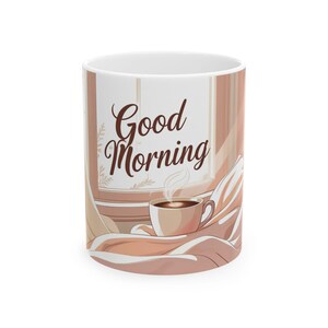 Könnte beinhalten: Weiße Keramik-Kaffeetasse mit umlaufender Illustration. Das Design zeigt eine warmtonige Illustration einer dampfenden Kaffeetasse vor einem Fenster mit dem Schriftzug "Good Morning" in Schreibschrift.