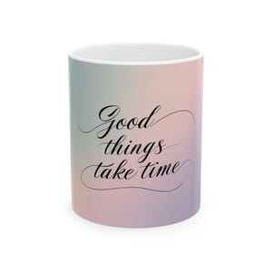 Könnte beinhalten: Eine weiße Keramik-Tasse mit einem Farbverlauf in Pastelltönen, mit dem Schriftzug "Good things take time" in schwarzer Schreibschrift. Die Tasse hat einen Standardgriff und eine glänzende Oberfläche.