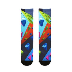 Könnte beinhalten: Ein Paar Socken mit einem farbenfrohen geometrischen Design, das an eine Kletterwand erinnert. Die Socken zeigen ein Muster aus blauen, grünen, roten und rosa Formen auf einem dunkelblauen Hintergrund. Die Socken haben schwarze Zehen.