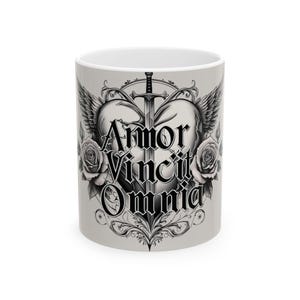 Könnte beinhalten: Weiße Keramik-Tasse mit einem schwarz-grauen Design. Das Design zeigt ein von einem Schwert durchbohrtes Herz, Flügel, Rosen und den Text "Amor Vincit Omnia."