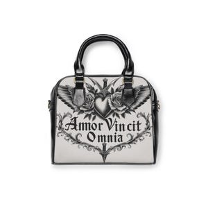 Könnte beinhalten: Schwarz-weiße Handtasche mit einem grafischen Design mit einem Herzen, Rosen, Flügeln und dem Text "Amor Vincit Omnia". Die Tasche hat schwarze Griffe und Verzierungen, mit einem Schulterriemen.