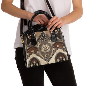 Könnte beinhalten: Schwarze und braune Handtasche mit floralem und architektonischem Muster. Die Tasche hat einen oberen Griff und einen Schultergurt. Das Design zeigt Brauntöne, Beige und Schwarz.