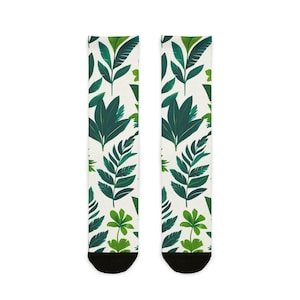 Könnte beinhalten: Ein Paar Socken mit einem sich wiederholenden Muster aus grünen Blättern auf weißem Hintergrund. Die Blätter variieren in Form und Größe, mit Schattierungen von dunkel- und hellgrün. Die Socken haben schwarze Zehen und ein botanisches Thema.