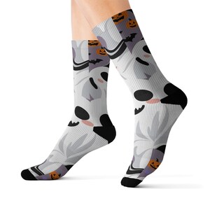 Könnte beinhalten: Weiße Socken mit einem sich wiederholenden Muster aus Cartoon-Geistern, Fledermäusen und Kürbissen. Die Geister haben schwarze Augen und Münder mit rosigen Wangen. Die Socken haben schwarze Fersen und Zehen, ideal für Halloween.