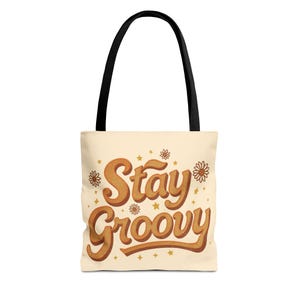 Peut inclure: Sac fourre-tout crème avec des anses noires. Il affiche l'inscription "Stay Groovy" en marron, dans un style rétro, ornée de fleurs et d'étoiles. Un accessoire de mode et pratique pour transporter des objets.