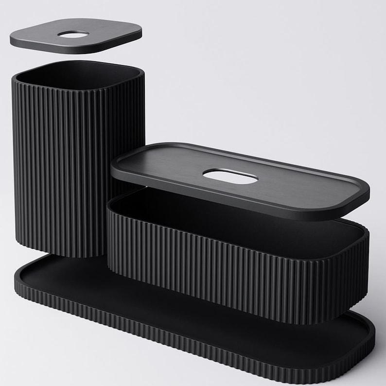 May include: A black, modern bathroom set featuring a tall, cylindrical wastebasket, a rectangular tissue box, and a long, rectangular tray. Each piece has a ribbed texture and a matte finish. The set includes a lid for the wastebasket and tissue box.