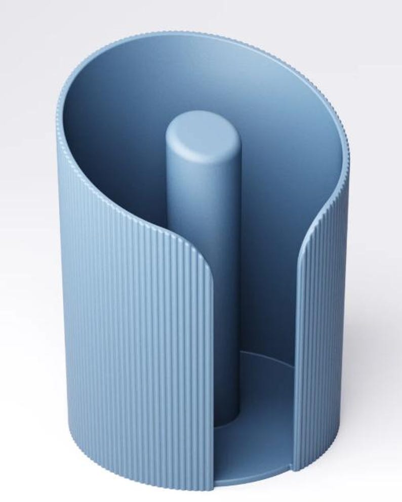 May include: A pale blue paper towel holder with a cylindrical design. The exterior has a vertical, ridged texture, and a central post. The holder has an open side for easy access to paper towels. The holder is made of a solid material.