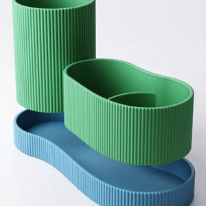 May include: A three-piece desk organizer set in shades of green and blue. The set includes a tall, cylindrical pen holder, an oval-shaped container, and a wavy-edged tray. All pieces have a ribbed texture, creating a modern, minimalist aesthetic.
