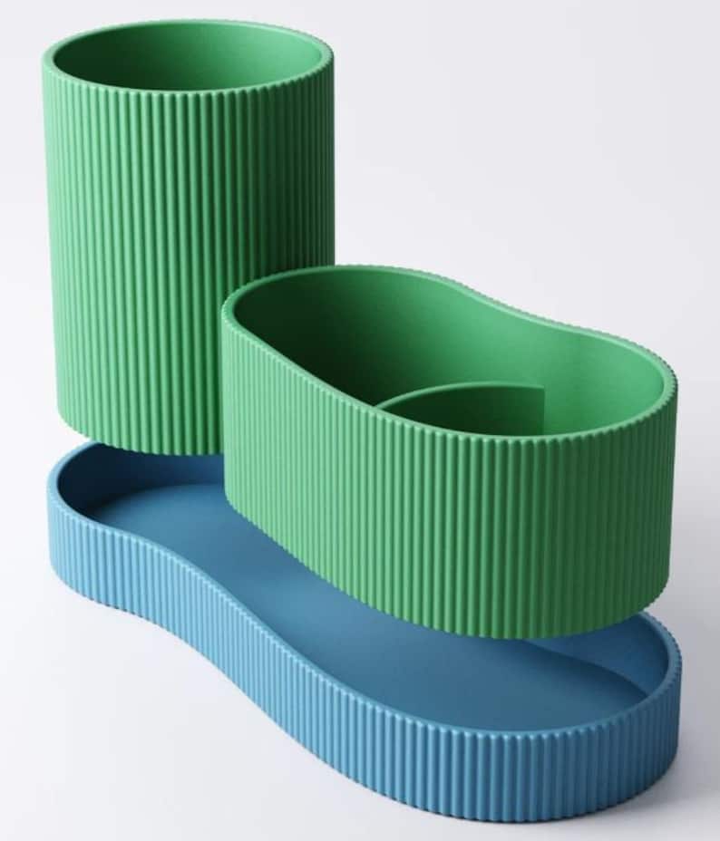 May include: A three-piece desk organizer set in shades of green and blue. The set includes a tall, cylindrical pen holder, an oval-shaped container, and a wavy-edged tray. All pieces have a ribbed texture, creating a modern, minimalist aesthetic.