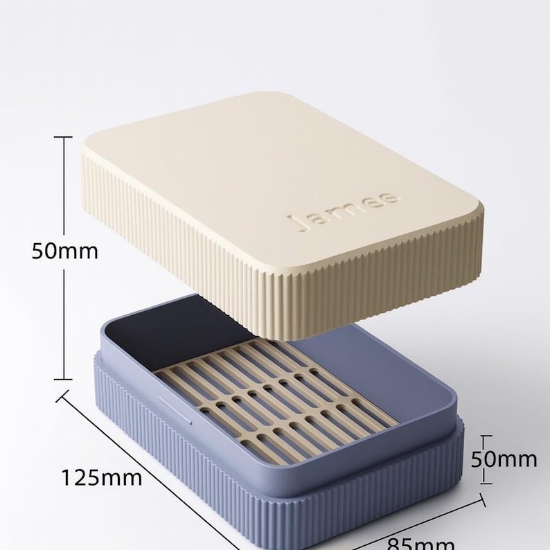 May include: A rectangular storage box with a cream-colored lid and a blue base. The lid has the name "James" embossed on it. The box is 50mm high, 125mm long, and 85mm wide. The interior has a beige tray with slots.