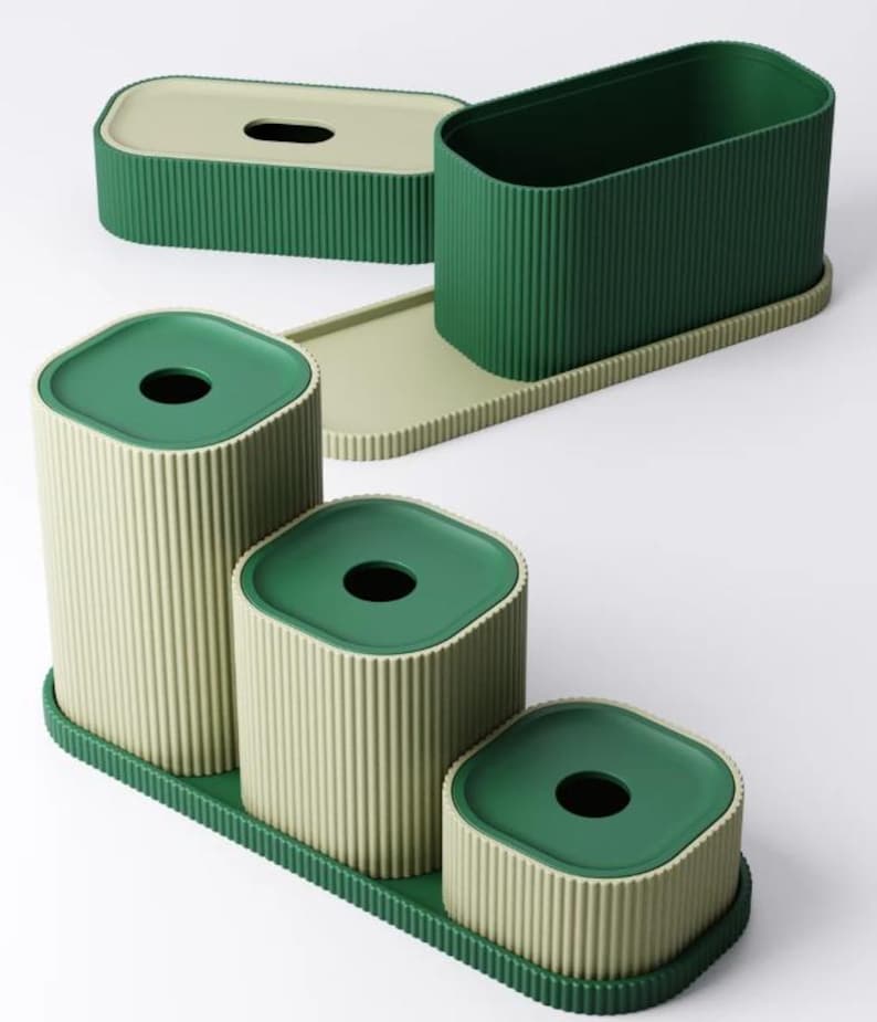 May include: A set of four green and beige ribbed containers. The set includes a rectangular tissue box, a tall open container, and three cylindrical containers with lids. The lids and the base trays are green.