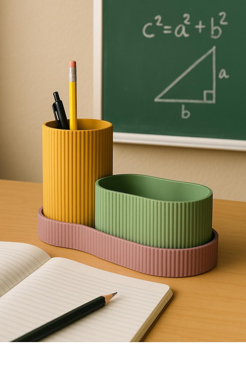 May include: A desk organizer set in yellow, green, and pink. The set includes a cylindrical pencil holder, an oval-shaped container, and a tray. A pencil and pen are in the yellow holder. A notebook and pencil are in the foreground. A chalkboard with a math formula is in the background.