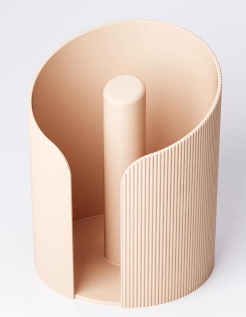 May include: A beige paper towel holder with a cylindrical design. It features a central post and a curved, ribbed outer surface. The holder has a minimalist, modern aesthetic with a smooth, matte finish. Designed to hold a standard roll of paper towels.