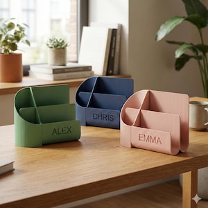 May include: Three desk organizers in green, blue, and pink, each with a ribbed texture. The green organizer has "ALEX" printed on it, the blue one has "CHRIS", and the pink one has "EMMA". They are on a wooden table.