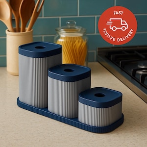 May include: A set of three gray and navy blue kitchen canisters with a ribbed design. The canisters are arranged on a matching tray. The image also includes a jar of pasta and a red circle with the words "FAST FESTIVE DELIVERY" and a truck icon.