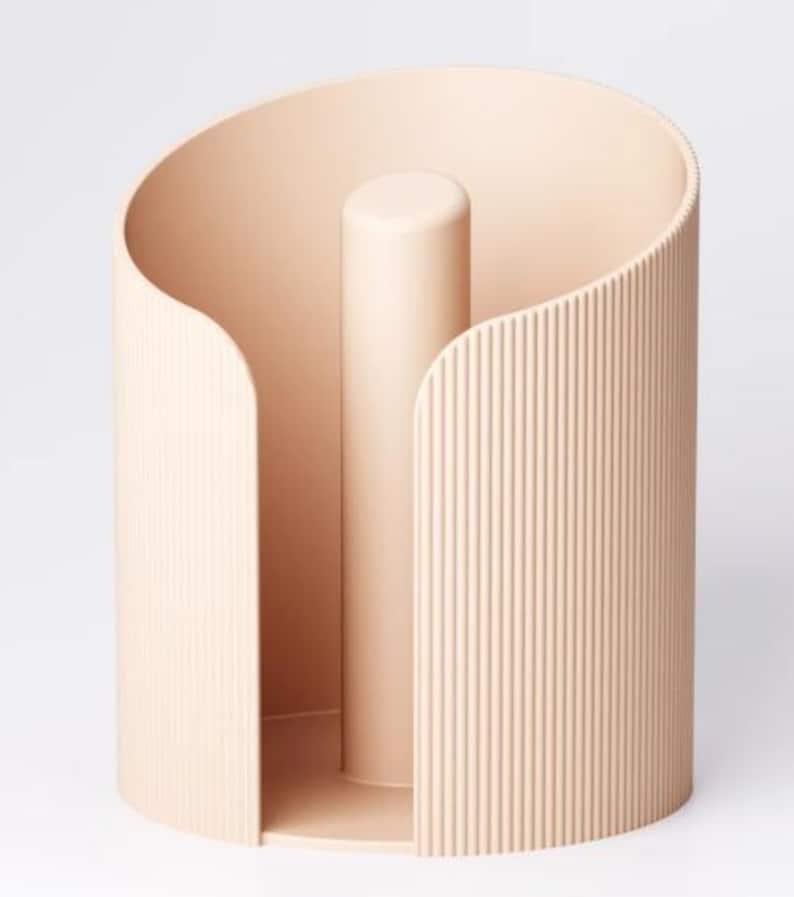 May include: A beige paper towel holder with a cylindrical design. The holder has a central post and a curved, ribbed exterior. The open design allows easy access to paper towels. The holder is made of a solid material.