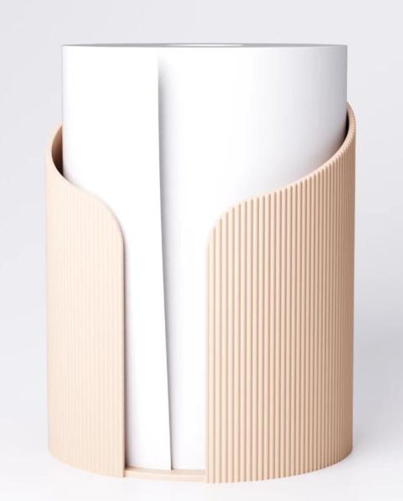 May include: A cylindrical paper towel holder with a light peach-coloured, ribbed exterior. The holder has a curved design that partially wraps around a roll of white paper towels, creating a modern and minimalist aesthetic.