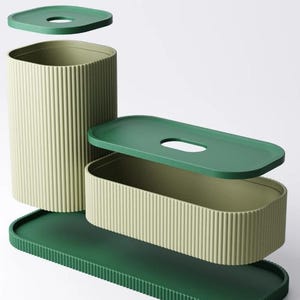 May include: A set of modern storage containers in shades of green. The set includes a tall, cylindrical container, a rectangular box, and a long tray, all with ribbed sides. Each container has a matching lid. The lids and tray are a darker green.