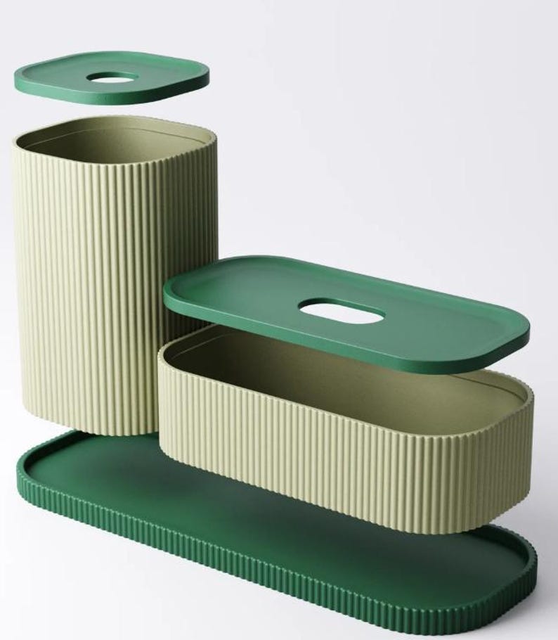 May include: A set of modern storage containers in shades of green. The set includes a tall, cylindrical container, a rectangular box, and a long tray, all with ribbed sides. Each container has a matching lid. The lids and tray are a darker green.