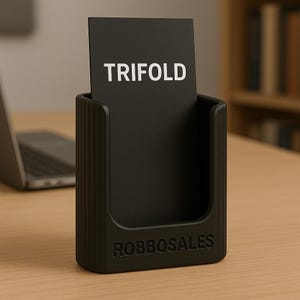 May include: A black business card holder with the word "TRIFOLD" in white text on a black card. The holder has the word "ROBBOSALES" embossed on the front. The holder is on a wooden surface.