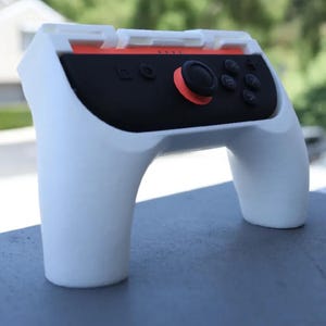 以下が含まれることがあります： 黒い中央部とオレンジ色のアクセントが付いた、白いゲームコントローラーグリップ。 コントローラーには、ジョイスティック、ボタン、十字キーがあります。 グリップは、ゲーム体験を向上させるように設計されています。