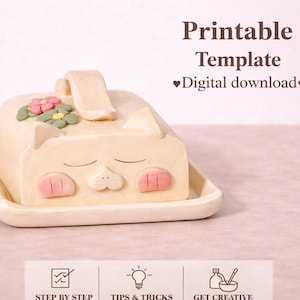 Könnte beinhalten: Eine beige Keramik-Butterdose in Katzenform mit geschlossenen Augen, rosa Wangen und einem Griff. Der Deckel ist mit rosa und grünen Blumen verziert. Die Worte "Printable Template" und "Digital download" sind im Hintergrund zu sehen.