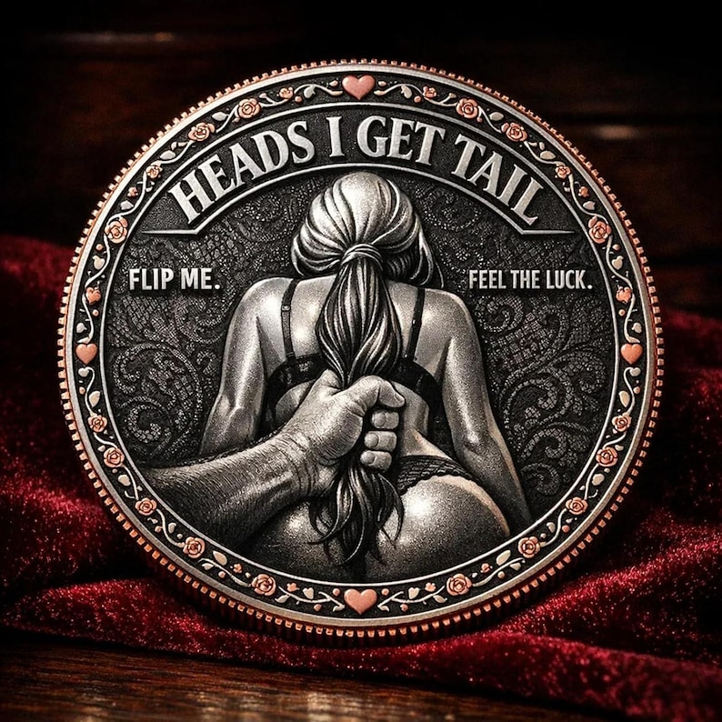 May include: A circular coin with a detailed relief design in silver tones. The coin depicts a woman's back with a hand holding her hair, and the text "HEADS I GET TAIL" and "FLIP ME. FEEL THE LUCK." are inscribed around the edge.