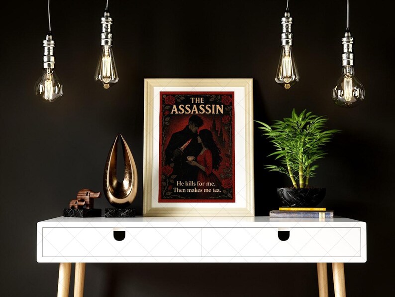 May include: A framed print titled "THE ASSASSIN" with a romantic illustration of a couple. The print is on a white table with decorative items and a plant. The text "He kills for me. Then makes me tea." is below the illustration.