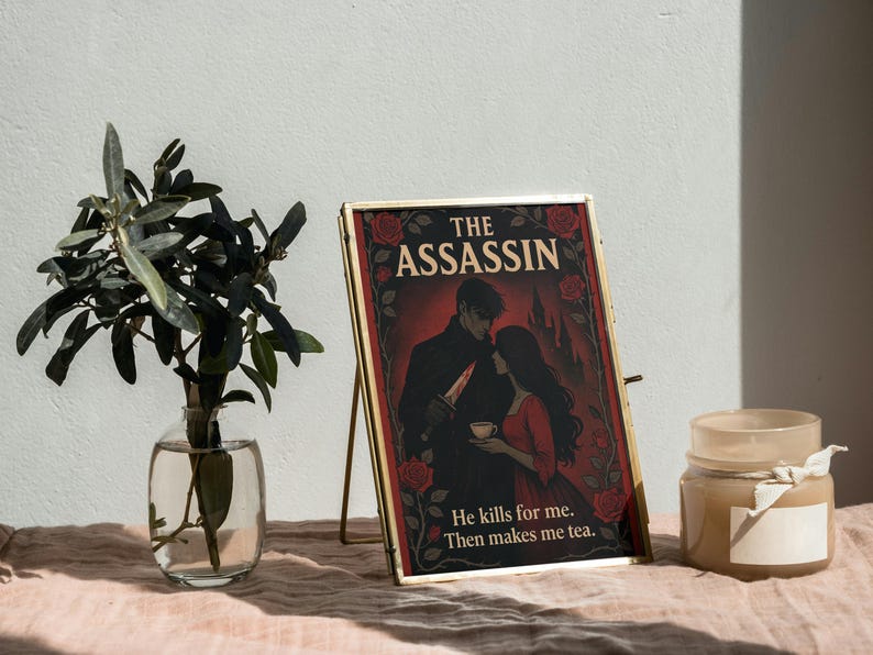 May include: A framed print with the title "The Assassin" features a romantic illustration of a couple. The artwork is set against a red background with rose accents. The text "He kills for me. Then makes me tea." is also included.