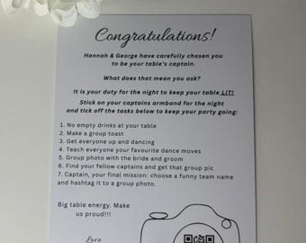 May include: A white card with black text, designed as a wedding party game. The card says "Congratulations!" and lists tasks for table captains, including taking a group photo. A camera graphic with a QR code is also present.