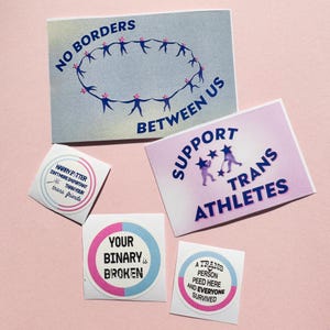 Peut inclure: Un ensemble de cinq autocollants et cartes avec divers motifs et textes. Une carte porte l'inscription NO BORDERS BETWEEN US avec des silhouettes en cercle. Une autre indique SUPPORT TRANS ATHLETES. Les petits autocollants mentionnent Harry Potter, le binaire et une personne trans.