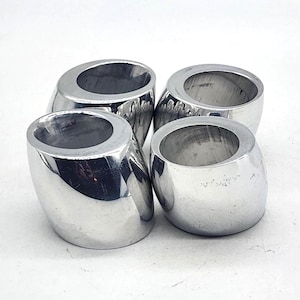 May include: A set of four polished silver-tone metal napkin rings. Each ring features a smooth, rounded, barrel-like shape with a slanted top opening. The metallic surface is reflective, showing highlights and shadows across the curved exterior.