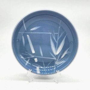 May include: A blue ceramic plate with a white bamboo leaf design. The plate has a white rim and is displayed on a clear stand. The bamboo design is a delicate, artistic touch, perfect for serving food or as a decorative piece.