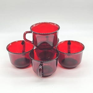 Può includere: Quattro tazze di vetro rosso rubino. Due tazze hanno manici e due no. Le tazze sono rotonde con un bordo leggermente svasato. Le tazze sono impilate a forma di piramide. Le tazze sono realizzate in un materiale di vetro trasparente.