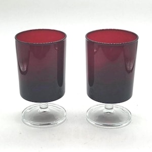 Può includere: Due calici con una sfumatura da rosso scuro a nero. I bicchieri hanno una forma cilindrica con una base trasparente e circolare. Il bordo del bicchiere è rosso vivo.