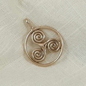 May include: A gold-toned pendant featuring a Celtic knot design with three intertwined spirals. The pendant is circular and has a loop at the top for attaching to a chain.