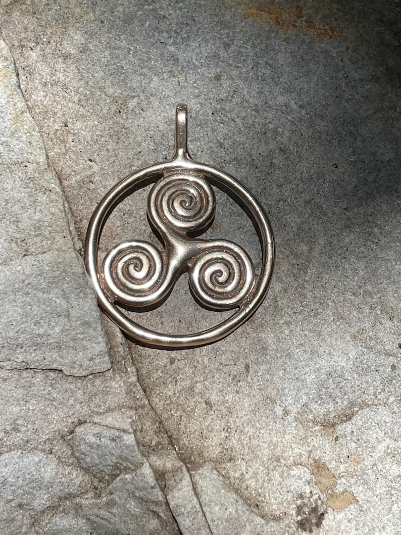 May include: A silver pendant featuring a Celtic knot design with three intertwined spirals. The pendant is circular and has a loop at the top for attaching to a chain.