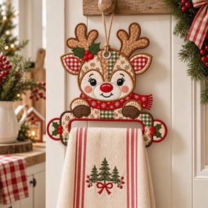 May include: A hanging kitchen towel holder shaped like a reindeer with a quilted fabric design in tan, red, and green. The reindeer features a red nose, a scarf, and holly accents. A cream-colored towel with red stripes and a tree embroidery hangs below.