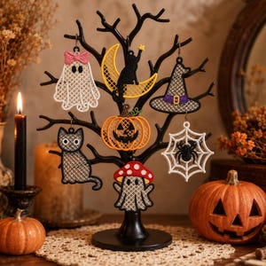 May include: A black metal tree display stand holding six embroidered Halloween ornaments: a white ghost with a pink bow, a black cat on a yellow crescent moon, a witch hat, a black cat, an orange jack-o'-lantern, and a white spider web.