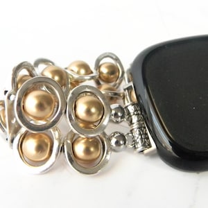 May include: A gold and silver beaded watch band with a black smartwatch. The band is made of small, round beads that are connected by silver rings.