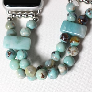 May include: A turquoise and silver Apple Watch band with a double row of beads. The beads are a mix of round and rectangular shapes, with some having a marbled pattern.