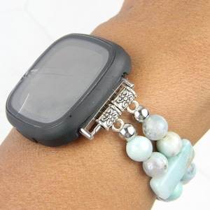 May include: A black smartwatch with a cracked screen is attached to a light blue beaded bracelet with silver accents.