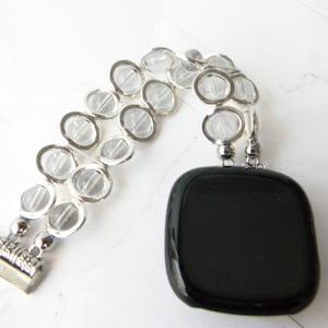 May include: A black square pendant with a silver chain made of clear glass beads.